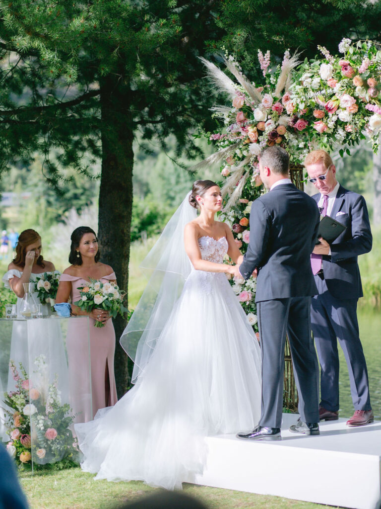 planning-a-destination-wedding-in-new-england bride and groom standing under a floral arch saying their vows while planning a destination wedding in New England