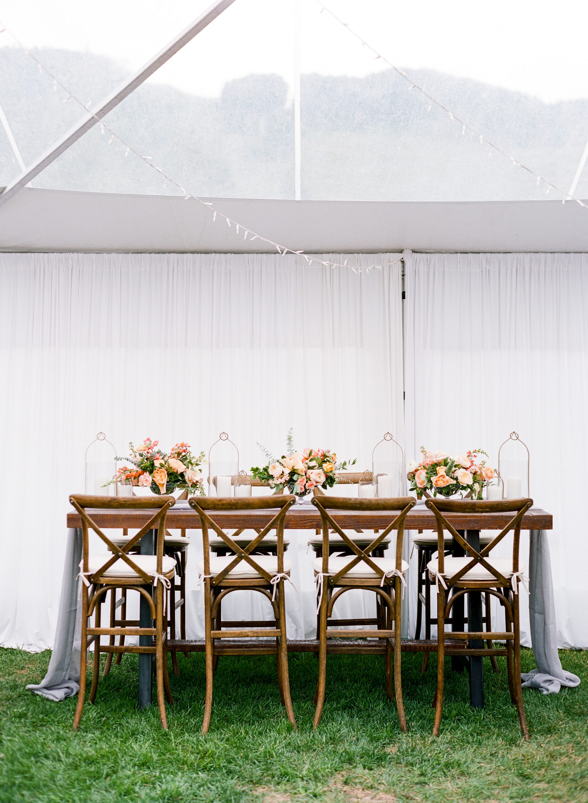 tented-wedding Chic wedding table with wooden chairs and floral centerpieces.