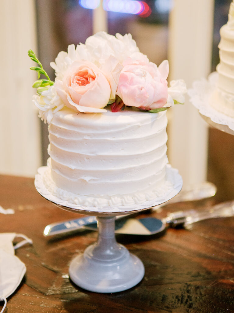 wedding-at-the-mount Small white wedding cake with textured buttercream frosting, topped with blush roses and peonies, displayed on a pale pedestal stand.