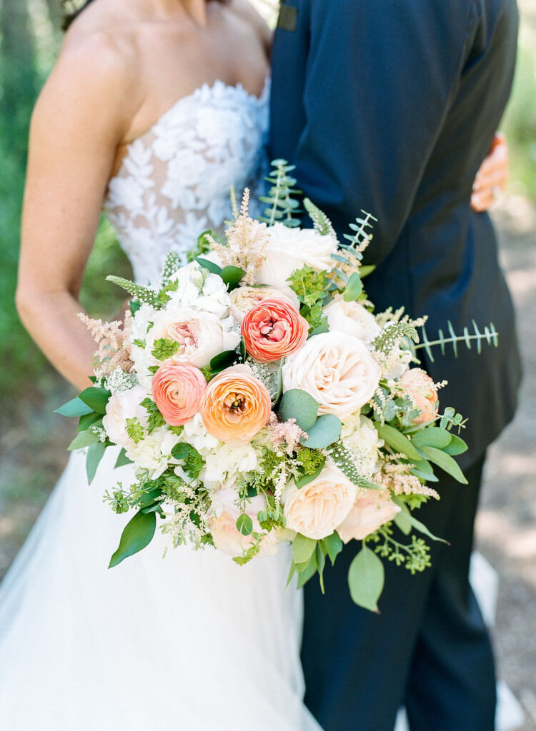 wedding-at-the-mount Bride and groom embrace outdoors during a Wedding at The Mount, with the bride holding a lush bouquet of garden roses, ranunculus, and greenery.