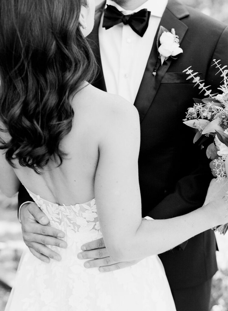 wedding-at-the-mount Black and white photo of a bride and groom embracing, showing the bride’s lace gown and the groom’s tuxedo with a boutonniere.