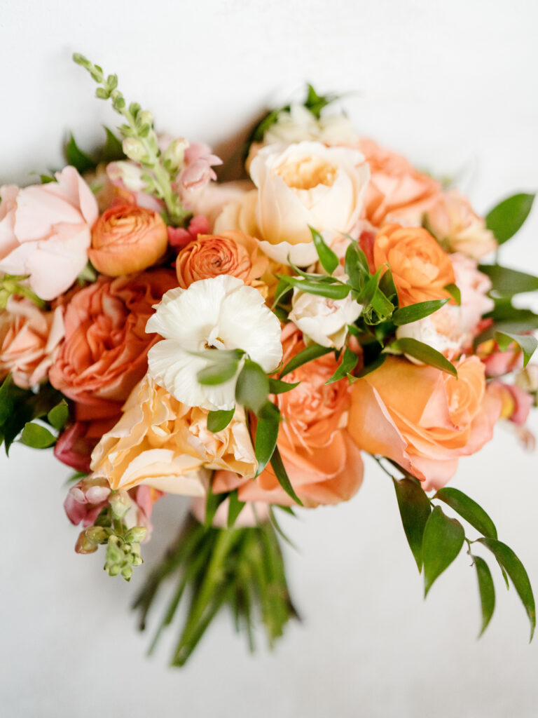 Vibrant bridal bouquet with peach, blush, and ivory garden roses and greenery, designed for a wedding at The Cliff House.