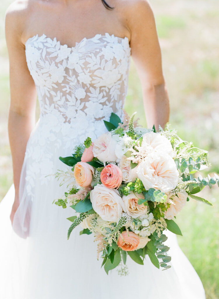 Bride in a strapless lace gown holding a romantic bouquet of blush and peach garden roses, captured during a wedding at The Cliff House.
