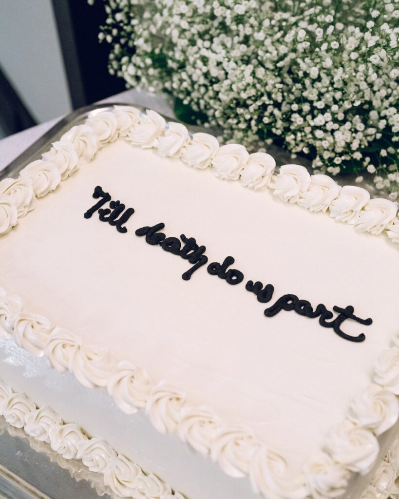 White wedding cake with scripted “Till death do us part,” ideal for romantic getaways in New England.