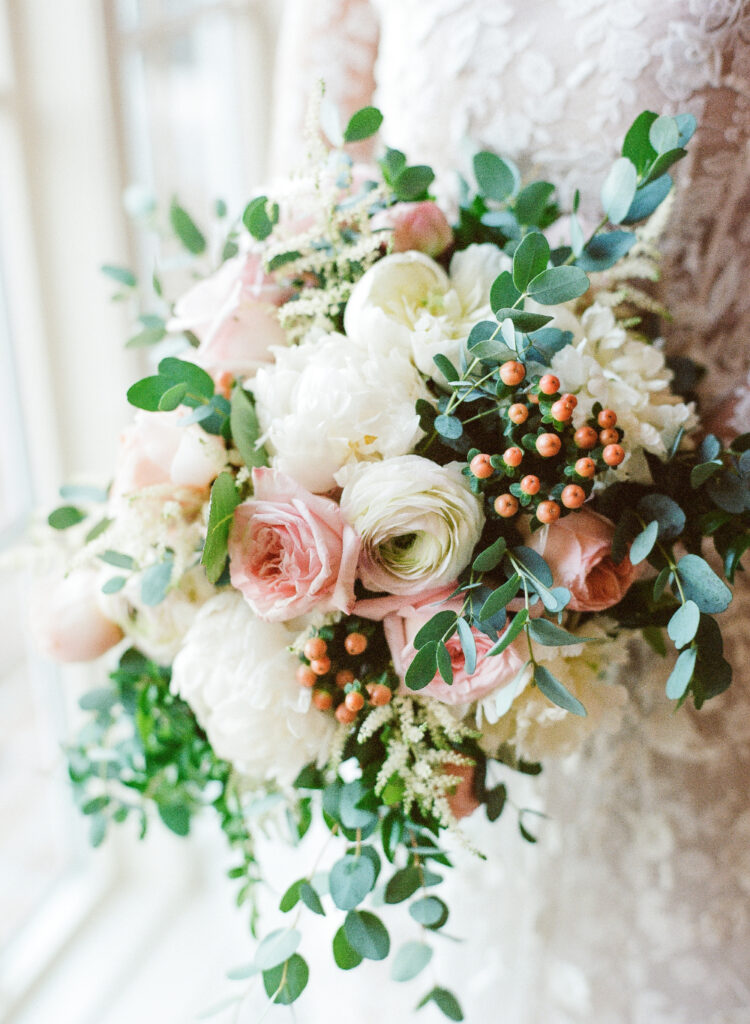 Bridal bouquet with white peonies, blush roses, ranunculus, berries, and eucalyptus.

