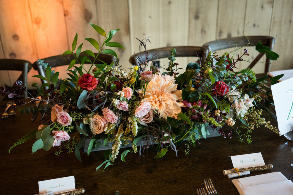 Lush centerpiece with rich wedding colors for a fall wedding featuring blush, burgundy, and greenery accents.