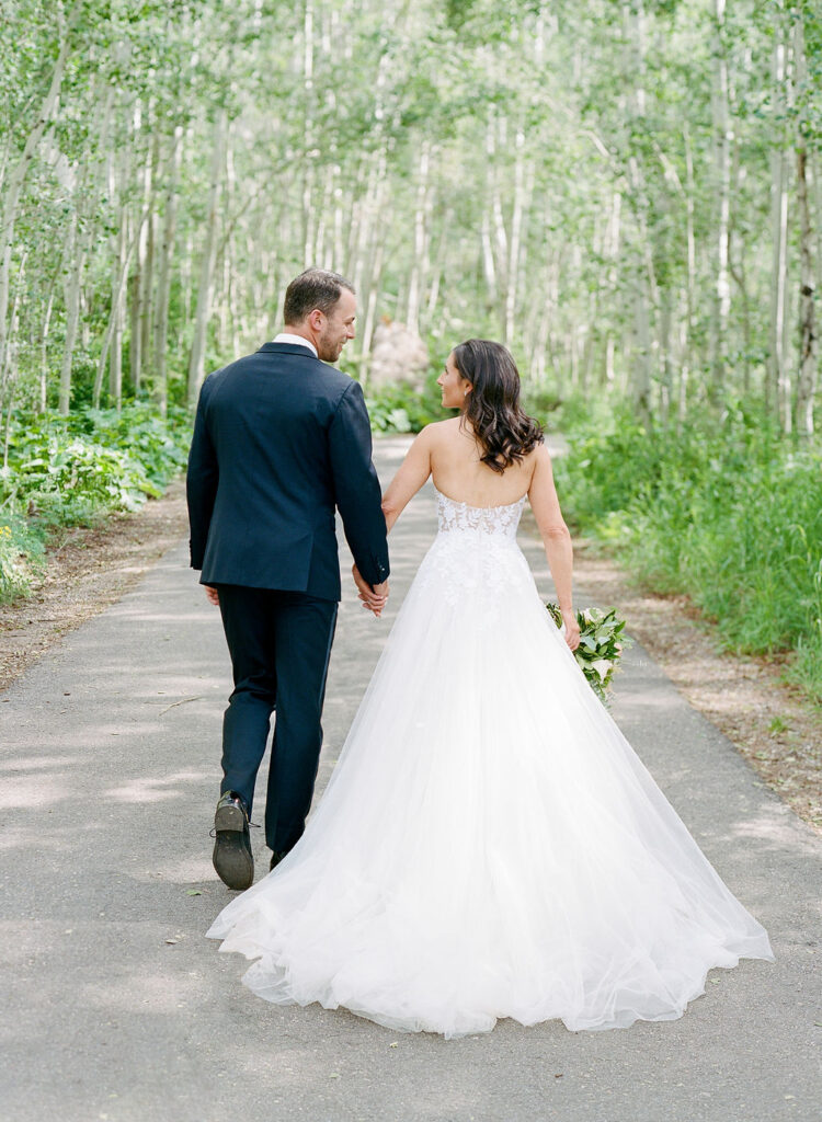 Bride and groom walk hand in hand through lush forest path, showcasing eco-friendly wedding tips in nature.