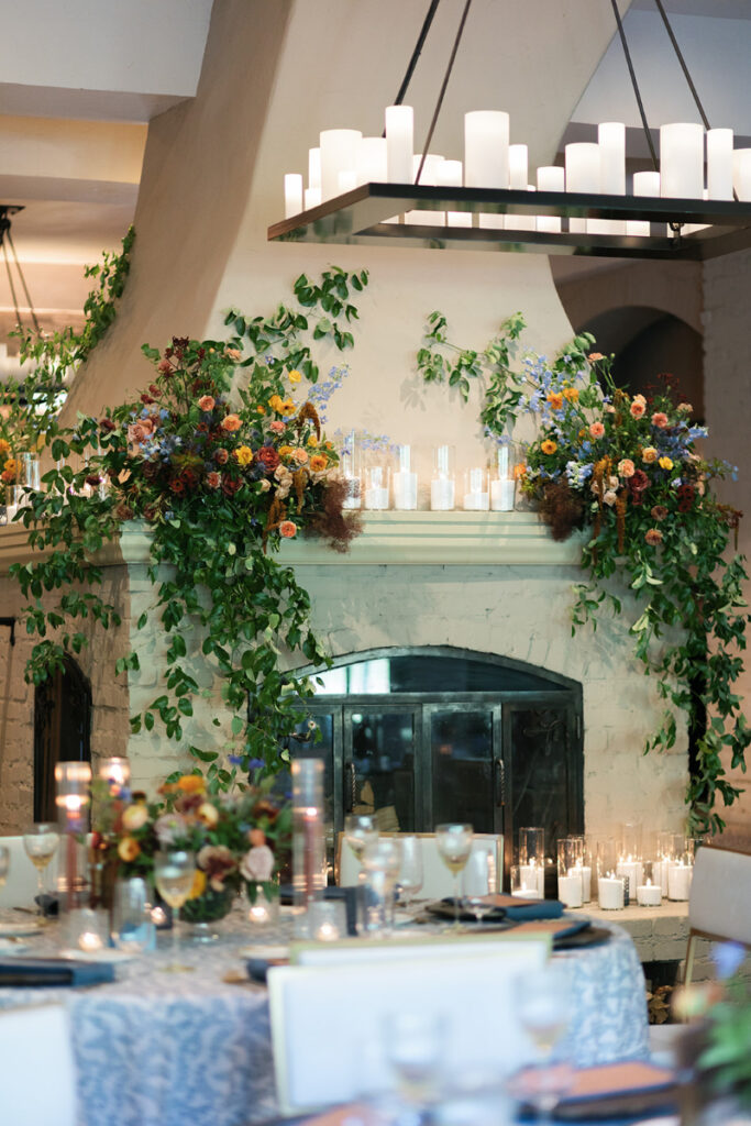 2026 wedding design trend featuring a floral-draped fireplace with greenery, taper candles, and romantic texture.