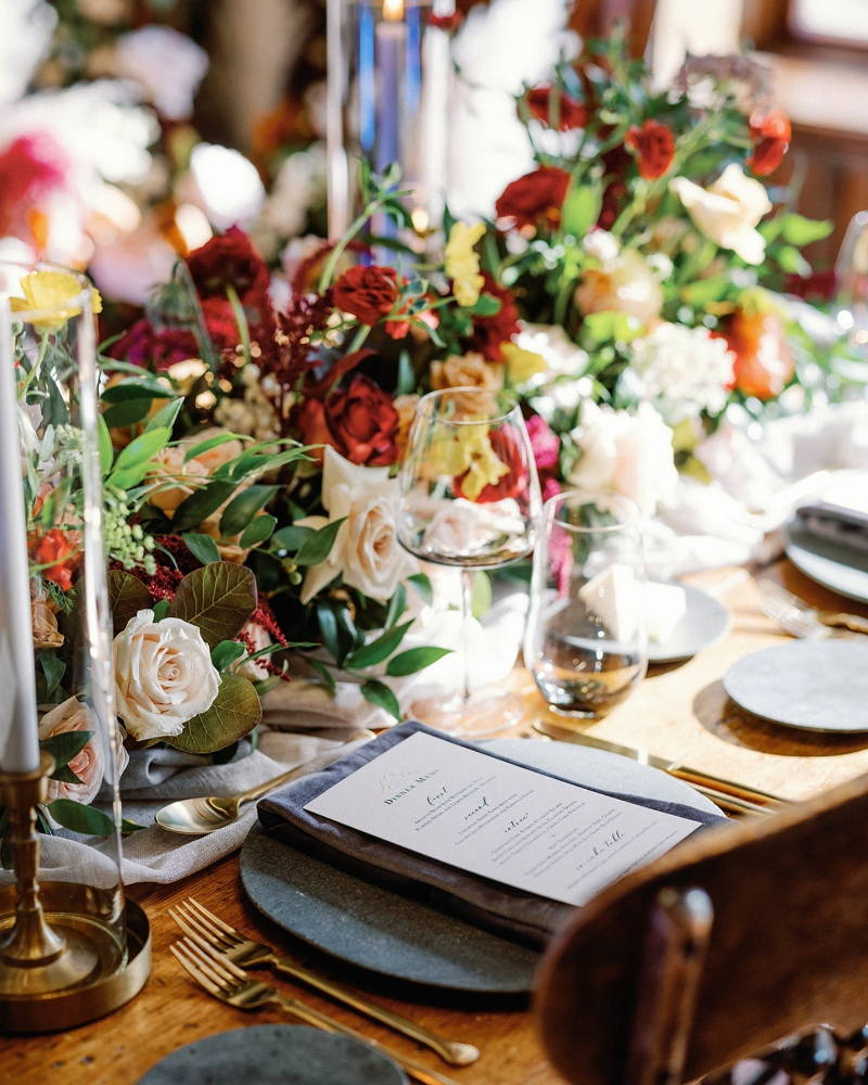 Lush floral centerpiece with warm tones and layered textures at a luxury fall wedding reception table.