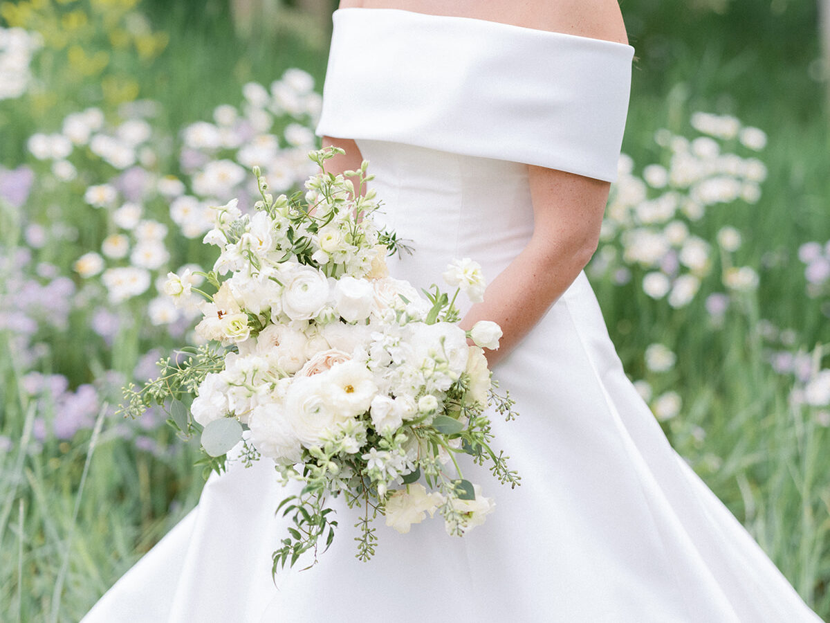 Bride holding white bouquet in wildflower meadow, showcasing timeless and elegant wedding design ideas.