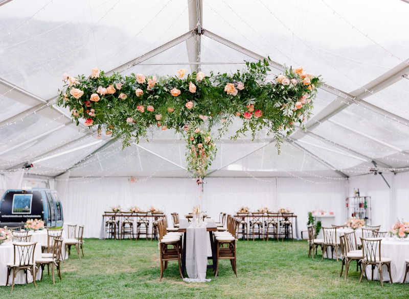 Tent wedding reception with floating floral chandelier, round and long tables, and soft garden-inspired design.