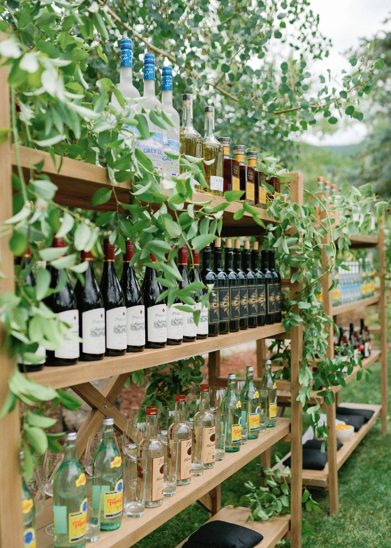 Wooden bar shelves with greenery and curated bottles showcasing thoughtful cocktail hour wedding design ideas.