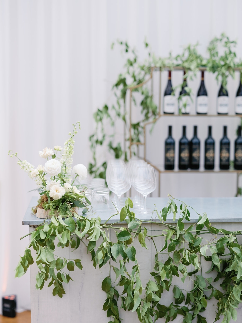 Wedding bar display with greenery garland, floral accents, and wine bottles for elevated wedding design ideas.