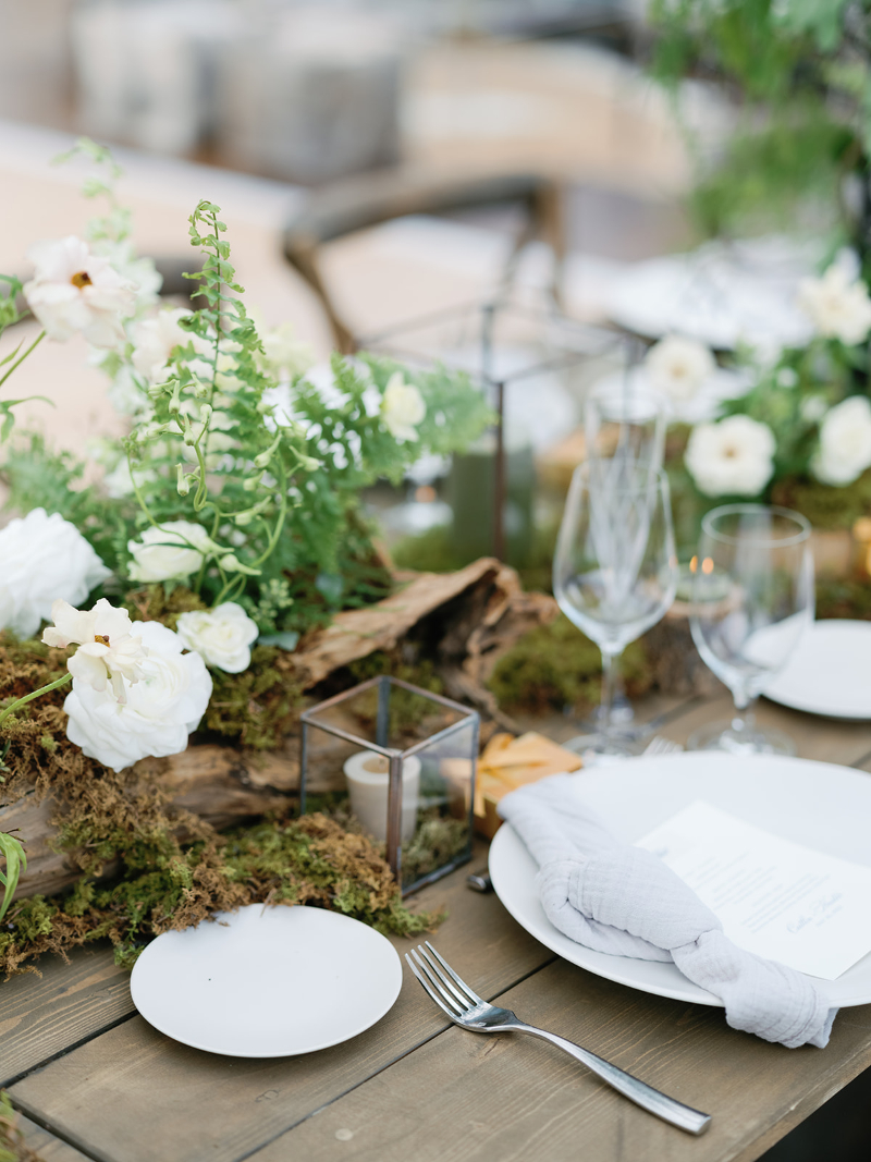Rustic wedding tablescape with white florals, moss, and candles for elevated wedding design ideas.