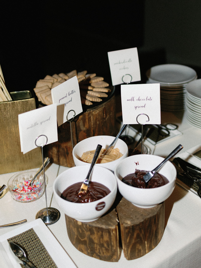 A s'mores bar display with chocolate spreads, peanut butter, cookies, and toppings in white bowls and jars.