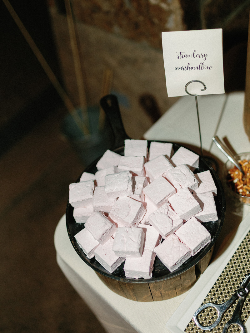 A bowl filled with pink strawberry marshmallows, placed on a wooden stand with a sign labeled "strawberry marshmallows."