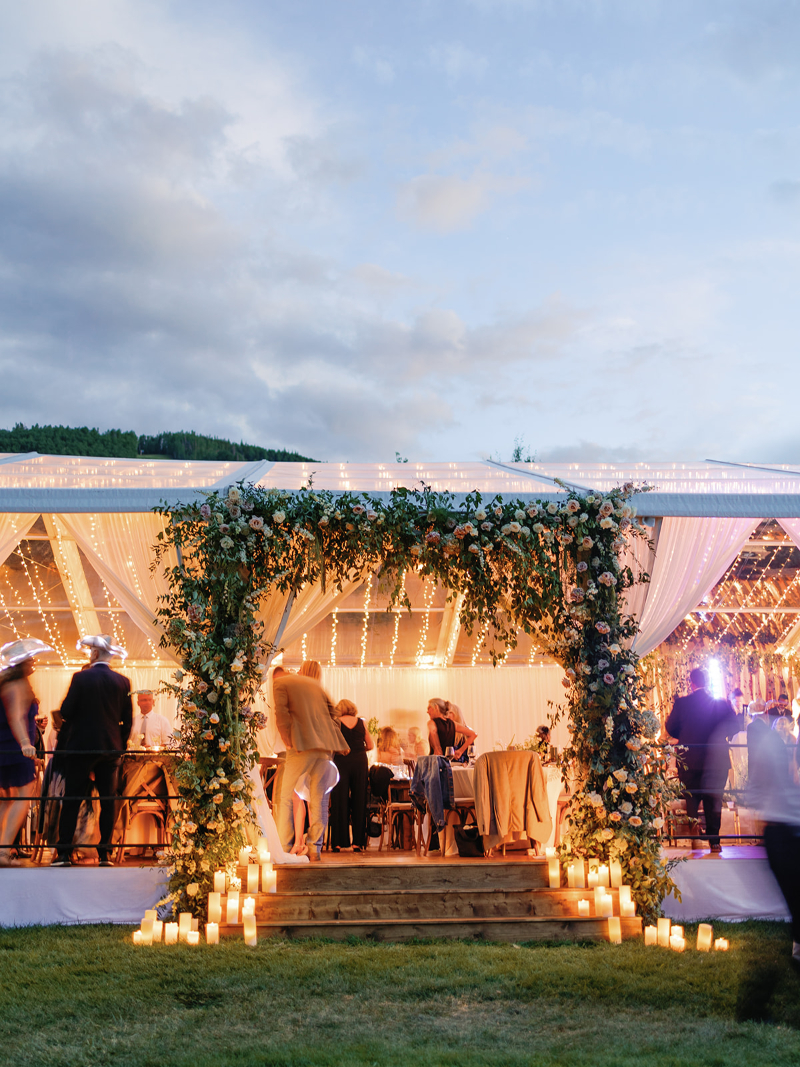 Guests mingle under glowing string lights at a romantic Colorado wedding tent entrance framed by florals.