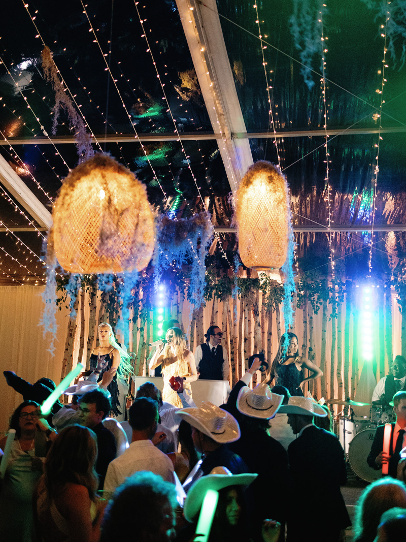 Live band performing under glowing lights and rattan pendants at vibrant Colorado wedding reception.