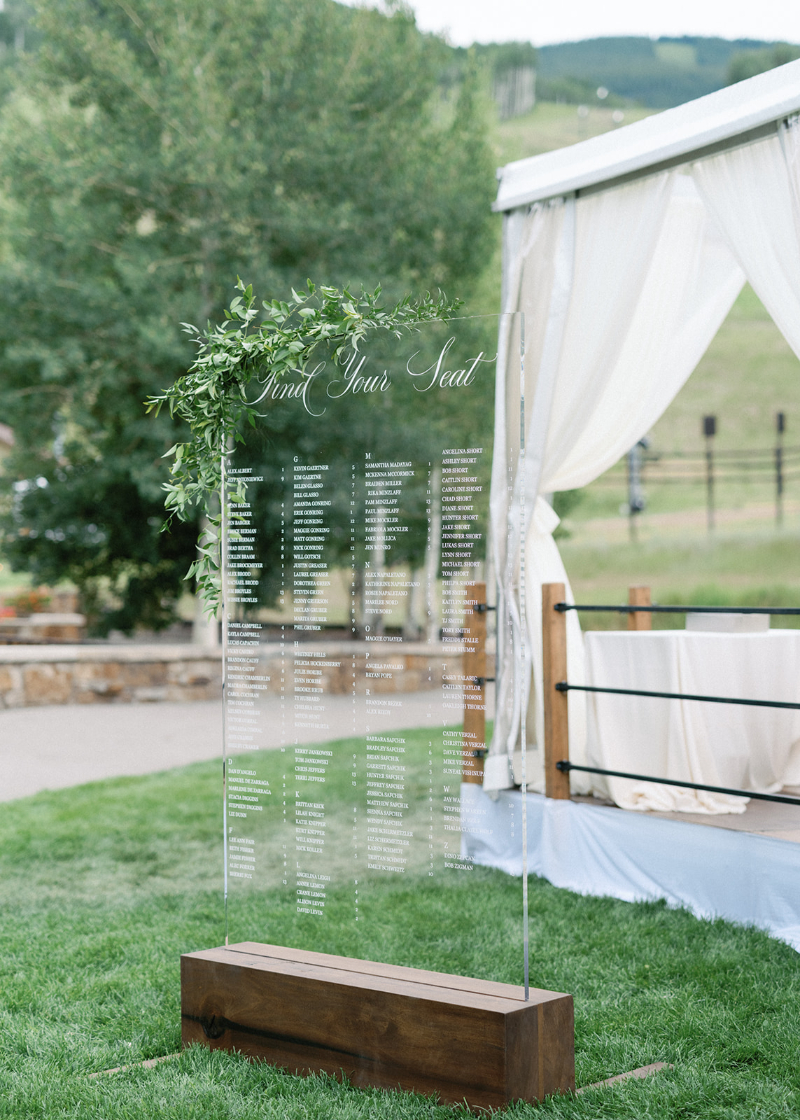 Acrylic seating chart with greenery and wood base, offering elegant and modern wedding design ideas.
