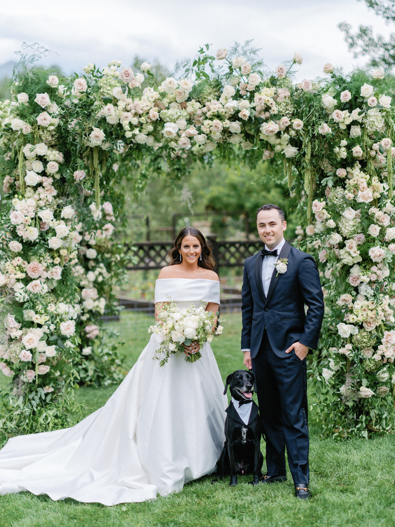 Bride and groom under floral chuppah with dog, highlighting timeless outdoor wedding design ideas.