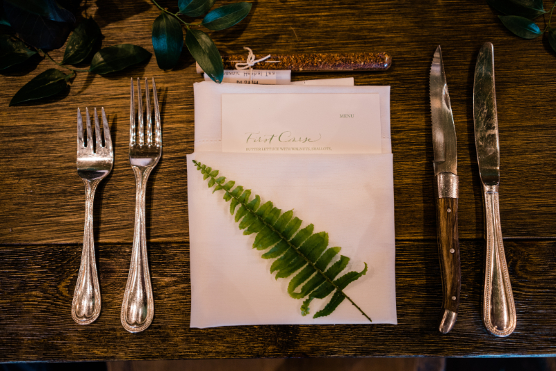 Nature-inspired wedding place setting with fern, menu, and vintage flatware to elevate the guest experience.