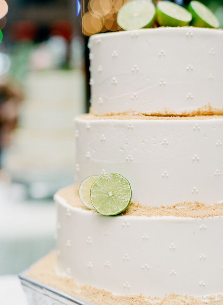 Two-tier white wedding cake with dotted buttercream, graham crumb edges, and fresh lime slice accents.