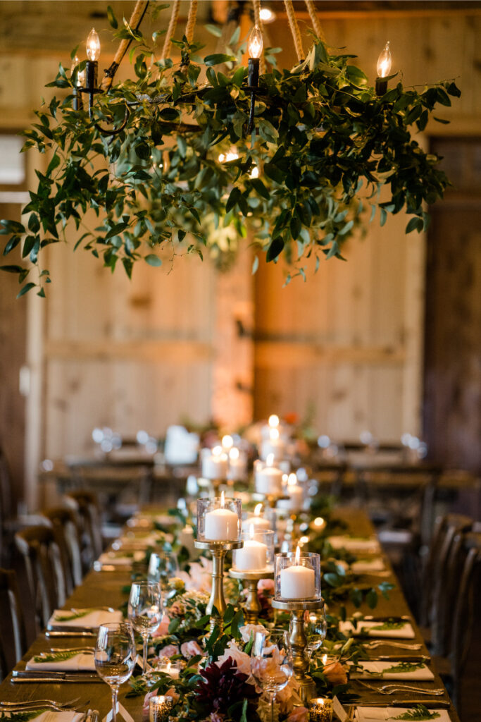 Overhead floral and drapery installations with greenery and candlelight create a warm, rustic reception setting.