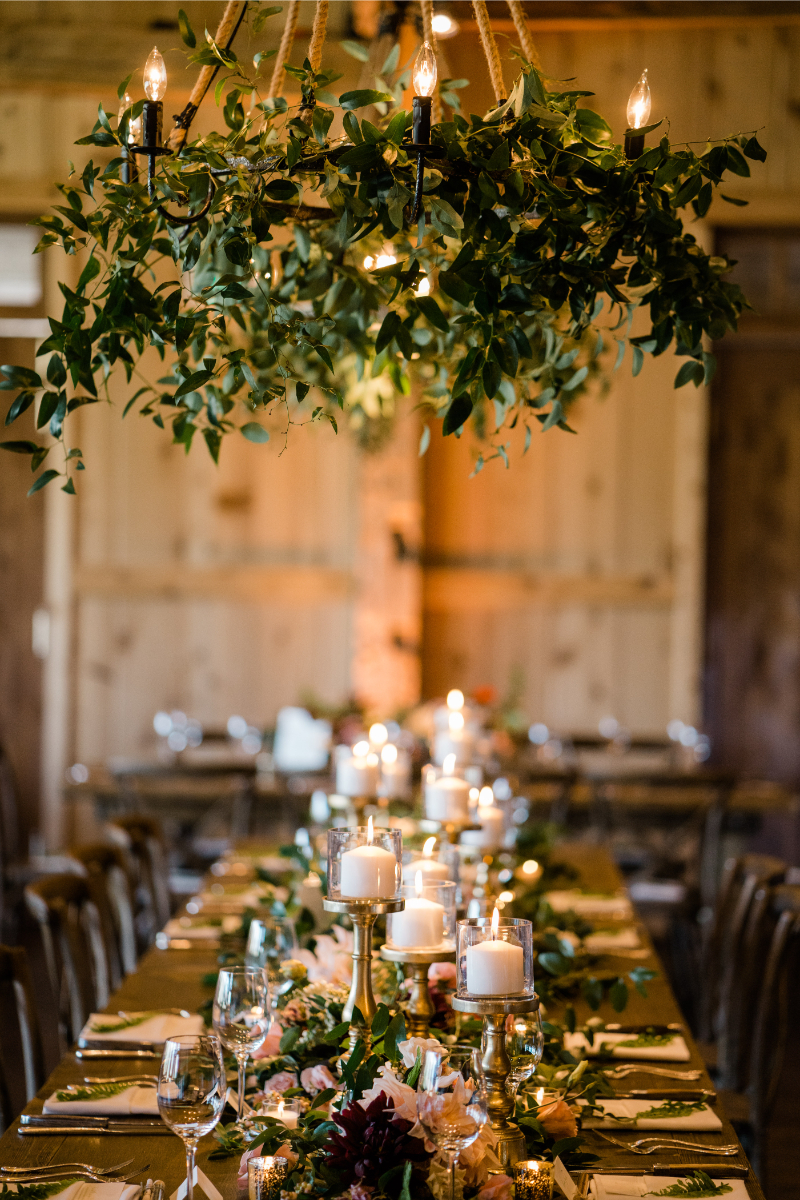 Overhead floral and drapery installations with greenery and candlelight create a warm, rustic reception setting.