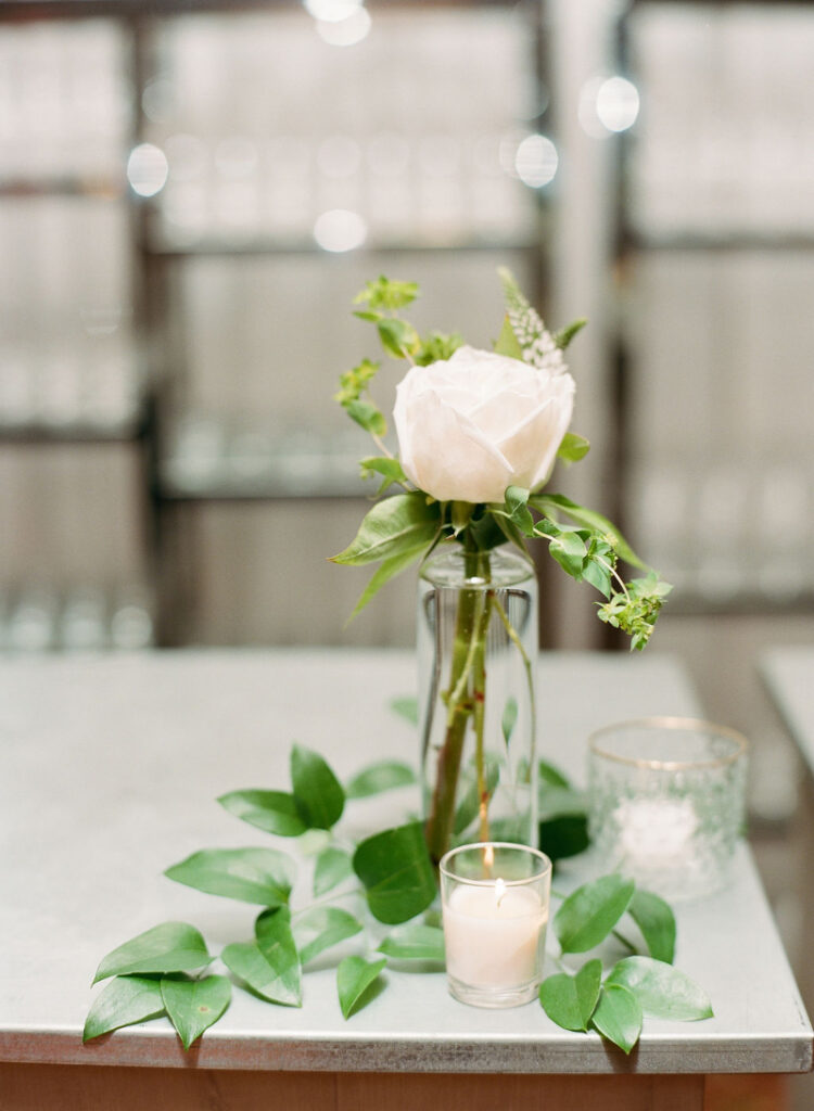 Single stem rose in glass vase with greenery and candle at Cape Cod wedding venue reception table.