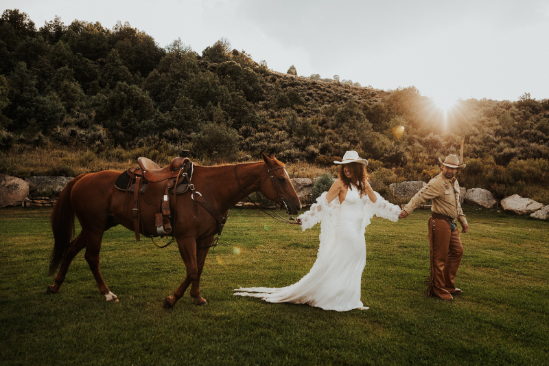 Bride walking beside horses during a scenic Colorado ranch wedding at Lazy J Ranch with open fields and mountain views.