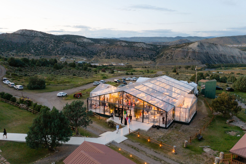 Clear-top tent reception glowing at sunset during a Colorado ranch wedding at Lazy J Ranch surrounded by mountain views.