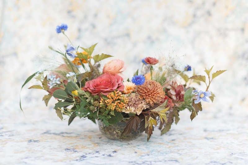 Low floral arrangement with soft peach, blue, and yellow blooms styled in an organic garden-inspired centerpiece
