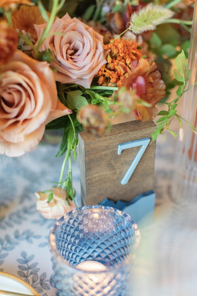 Elegant table setting with soft florals, wood table number, and blue glass candle detail