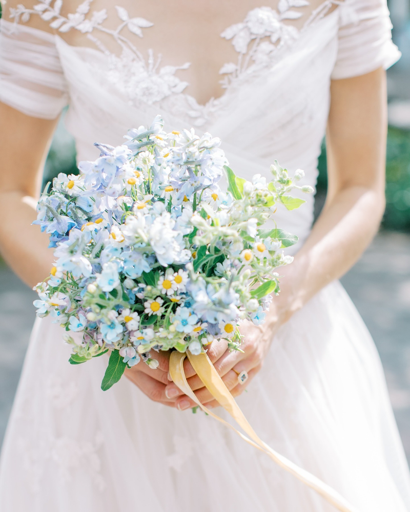 Spring wedding color palettes with soft blue bouquet and delicate blooms held by bride in natural light