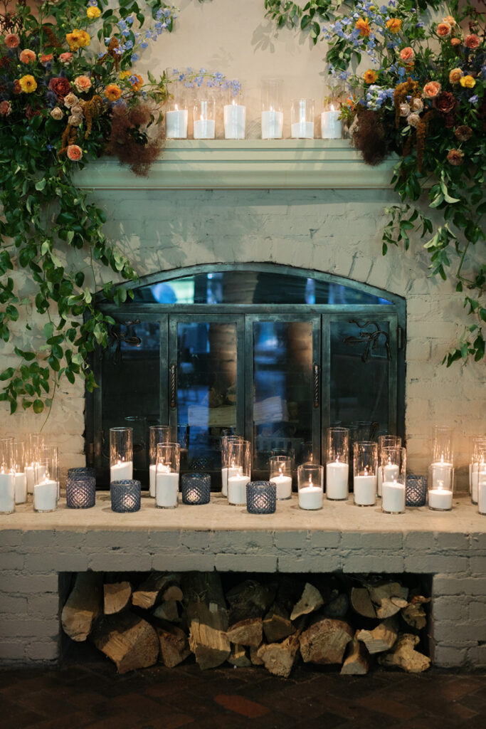 Romantic fireplace mantel with lush floral arrangements, soft candlelight, and elegant greenery cascading indoors.