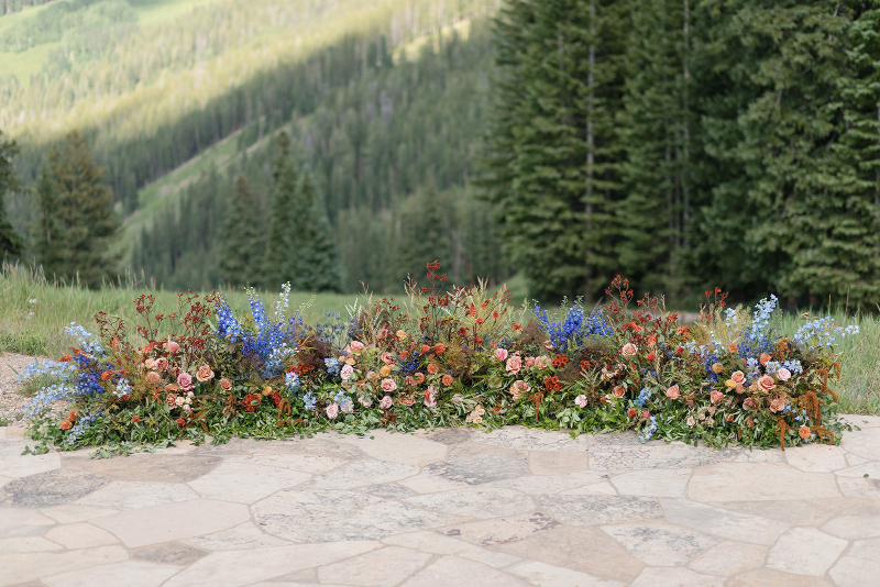 Mountain ceremony florals with colorful wildflower arrangements and lush greenery overlooking a scenic forest landscape.