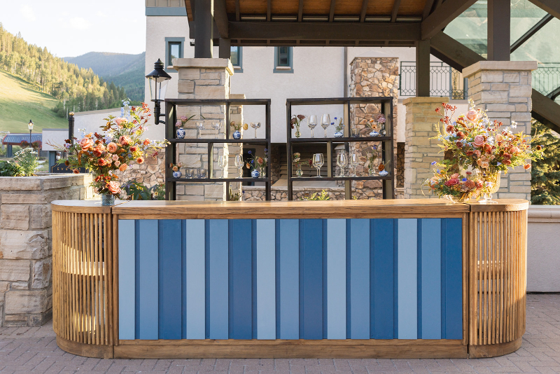 Modern outdoor bar setup with colorful floral arrangements, mountain views, and elegant cocktail hour styling.