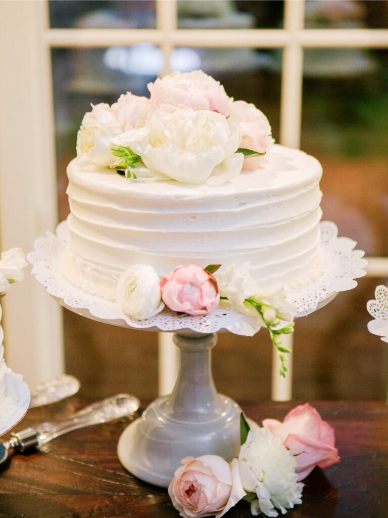 Elegant white wedding cake with soft frosting texture and fresh blush and ivory floral accents on display stand