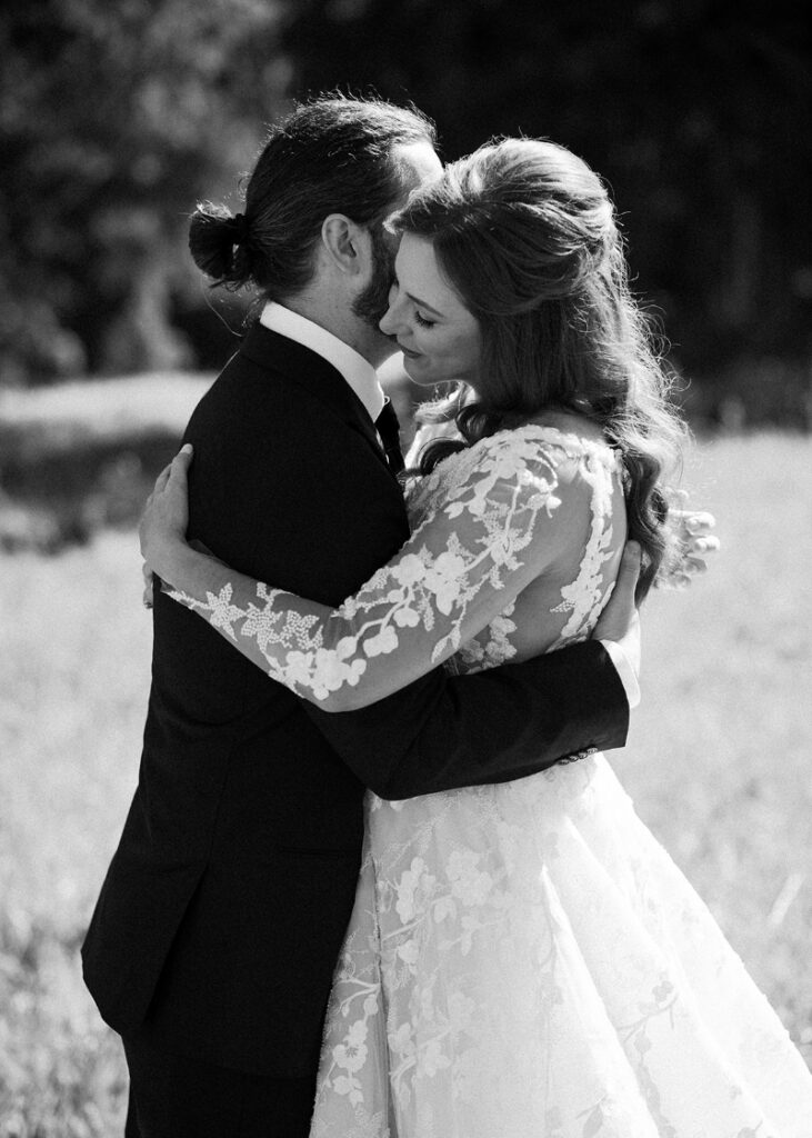 Black-and-white portrait of newlyweds embracing outdoors, capturing a quiet and intimate wedding moment.