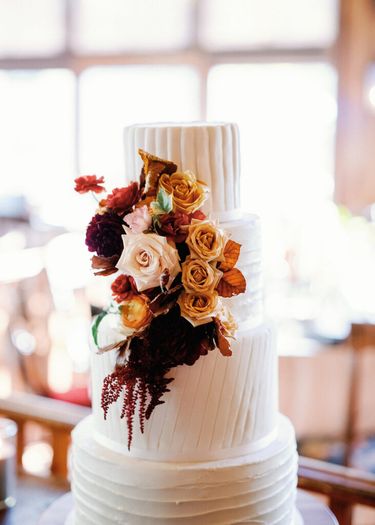 Elegant white wedding cake adorned with cascading roses and rich seasonal floral accents.
