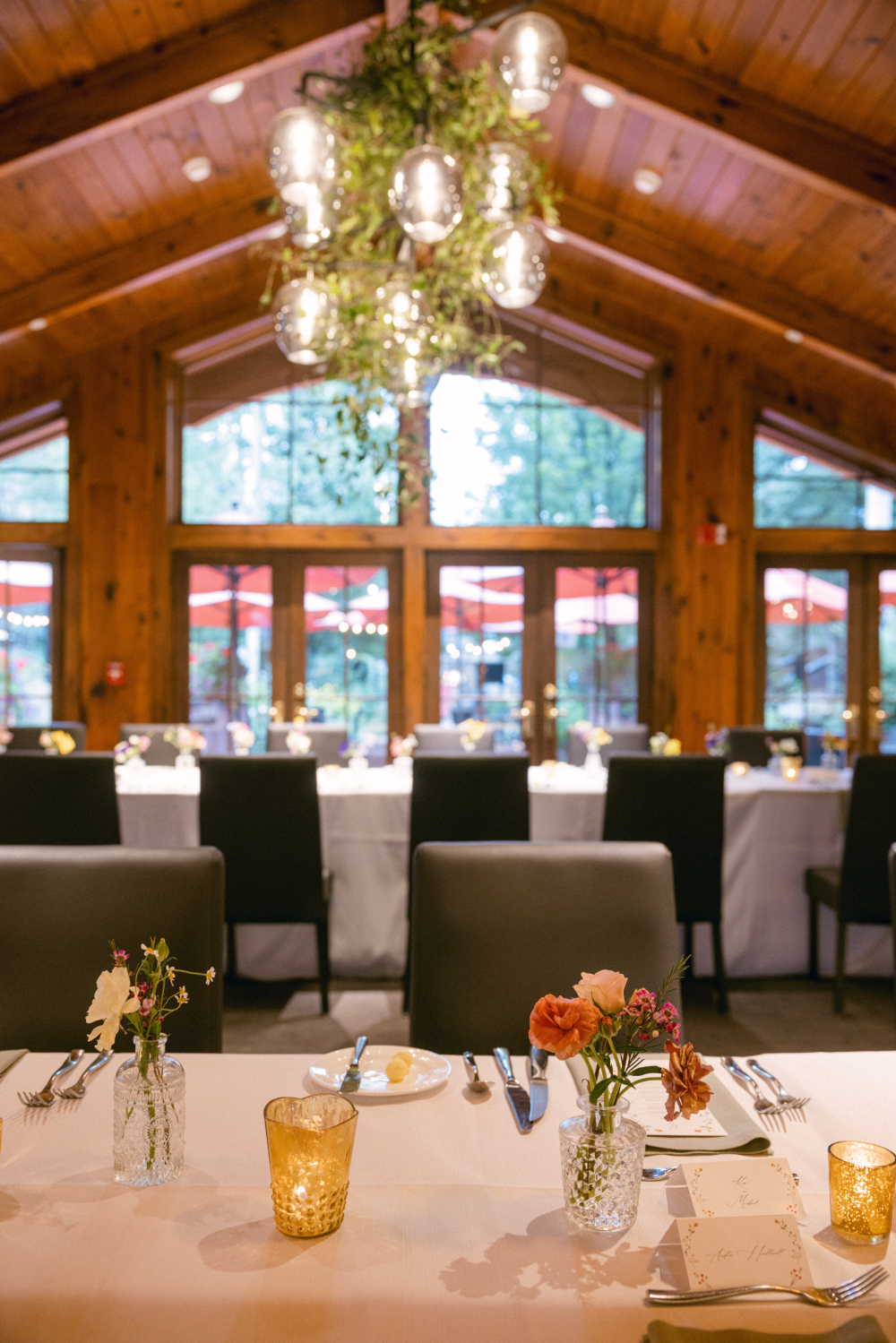 Soft candlelight, delicate florals, and modern furnishings create an intimate reception atmosphere. Floor-to-ceiling windows bring the outdoors in, blending natural beauty with understated elegance for a memorable evening.