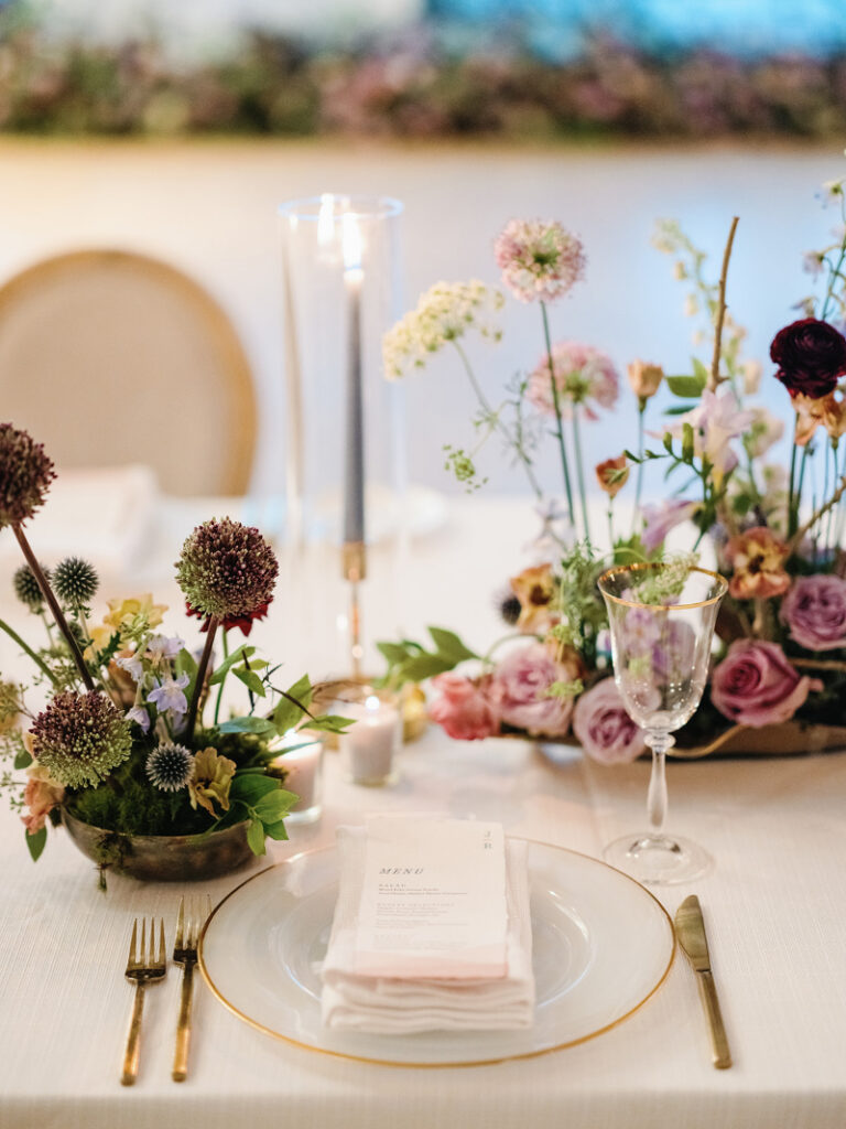 Elegant reception table with layered florals, candlelight, and place setting supported by thoughtful luxury wedding logistics.