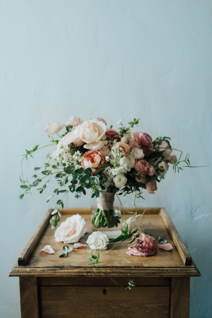 Romantic bridal bouquet with soft pink and white flowers arranged on a vintage wooden table.